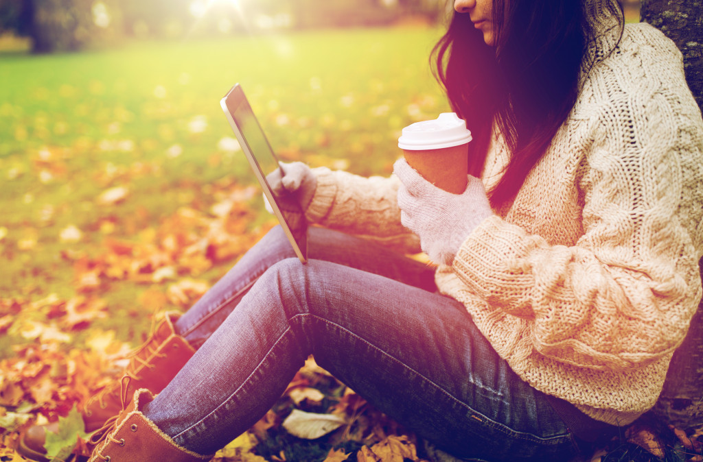 a girl sitting outdoors is using her laptop while holding a coffee cup