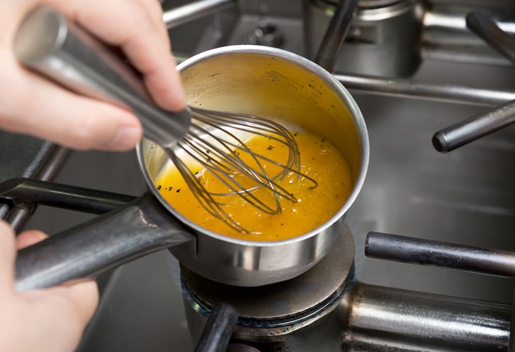 A person using a whisk to cook and stir chicken stock