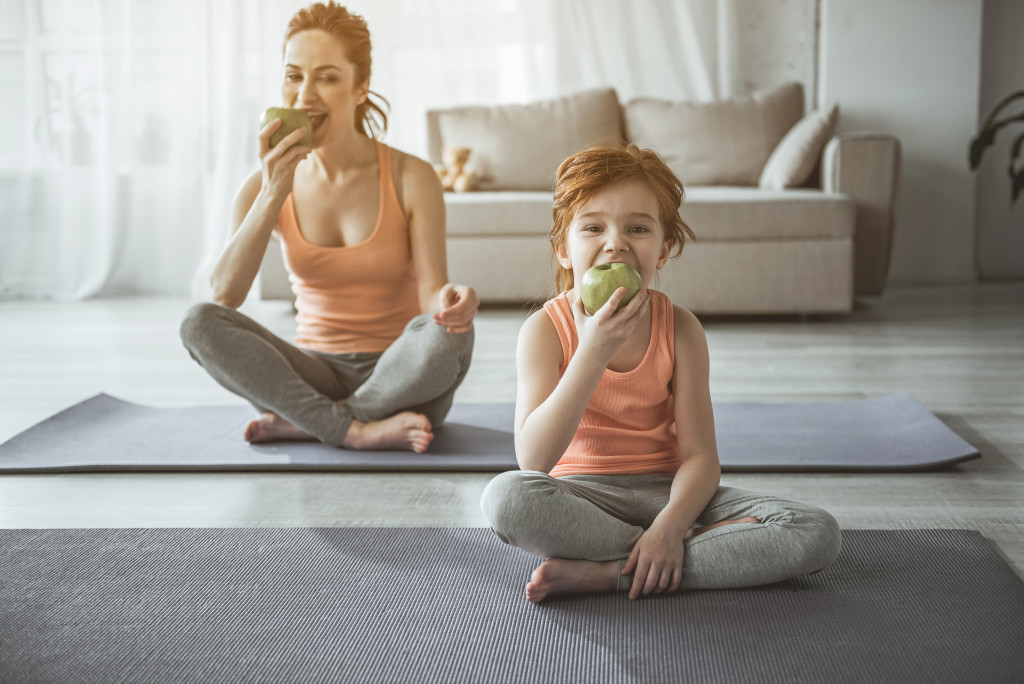 Full length portrait of woman and child sitting on carrymats and eating juicy fruits