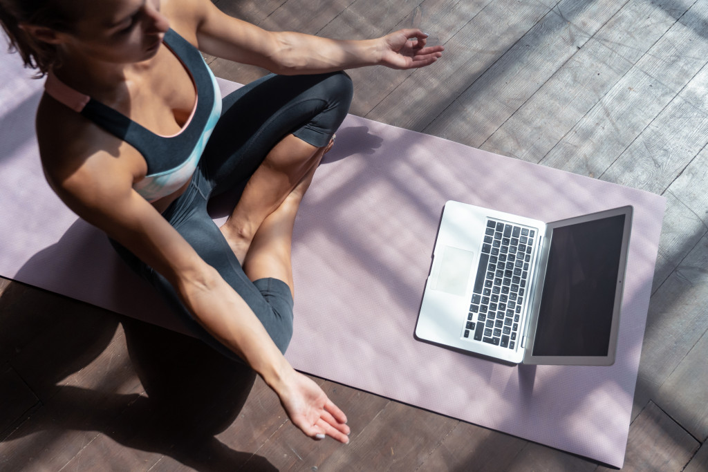 woman meditating in yoga mat at home with laptop in front of her