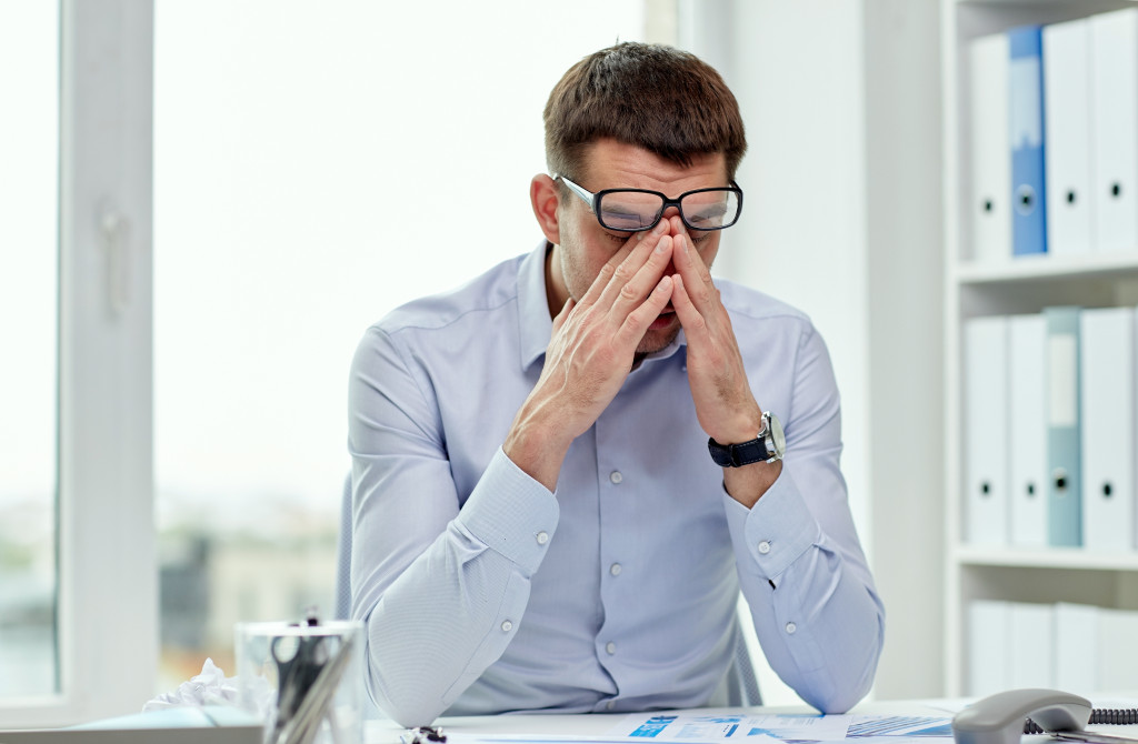 A stressed out businessman or worker in the office, rubbing his eyes