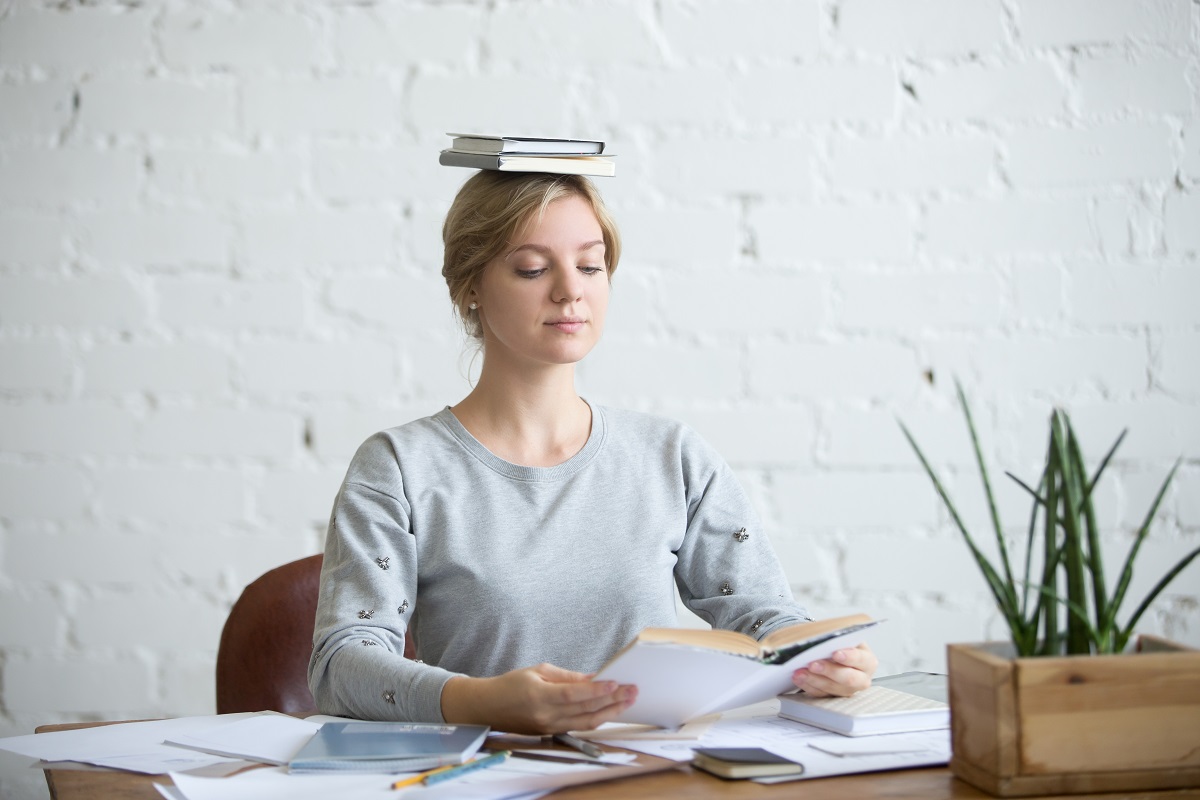 A woman sitting up straight with books on her head